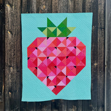 Load image into Gallery viewer, A quilt of a giant patchwork strawberry on a bright background. Quilt is hanging on the side of a wooden garage.

